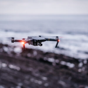 Modern drone with shining lights flying on blurred background of sea and coast